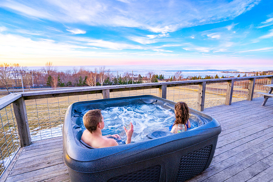 Two people overlooking the ocean in an outdoor hot tub at the Steinhart Distillery Cottages, Arisaig, Northumberland Shore